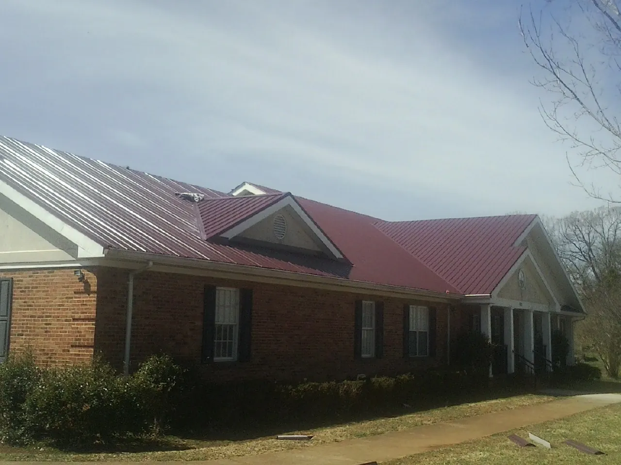 Red metal roof with gabled entries on a long brick building, from a Hail Damage Roof Repair job in Fort Calhoun