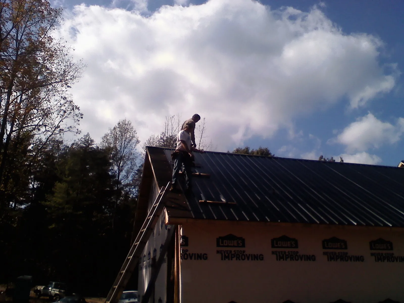 Roofer fastening dark metal panels high against a cloudy sky, from a Roof Inspection job in Fort Calhoun