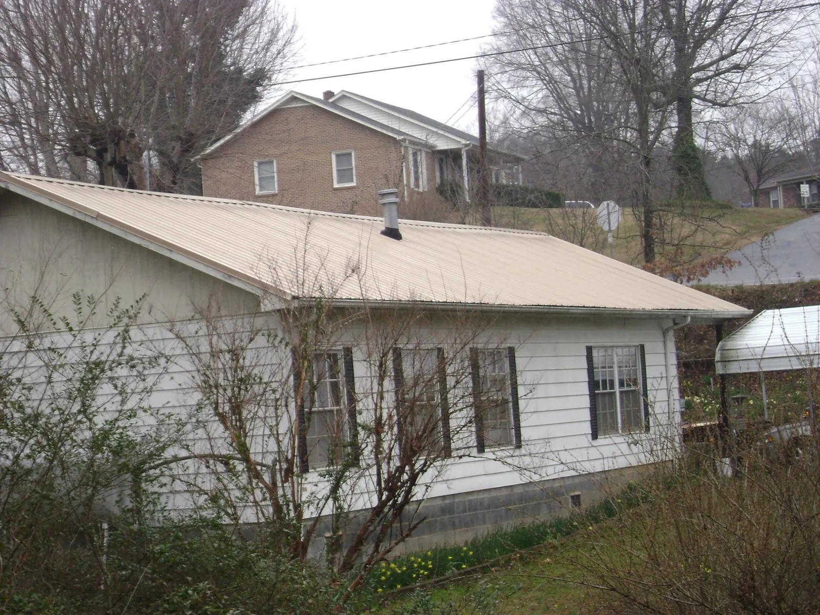 Tan metal roof on a white sided house set into a hillside — Commercial Roofing by Roofing Brothers in Fort Calhoun
