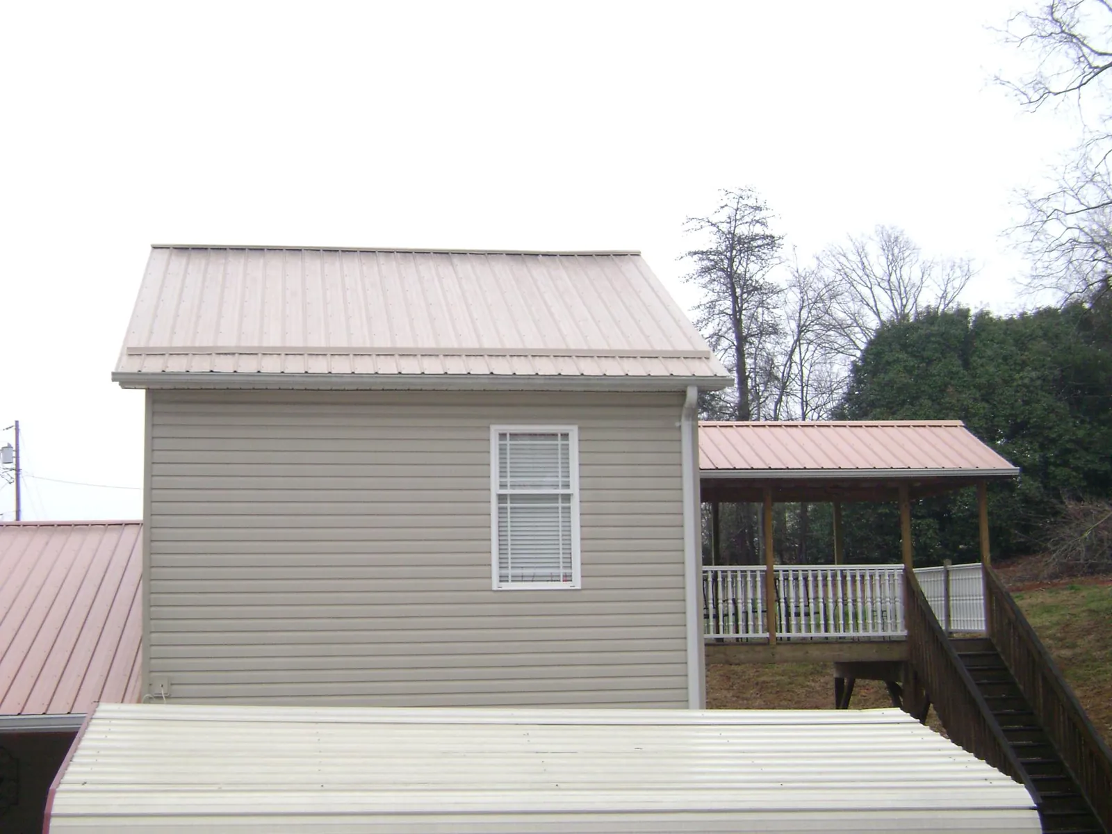 Tan metal roofs on a two story addition and attached porch, from a Roof Replacement job in Fort Calhoun